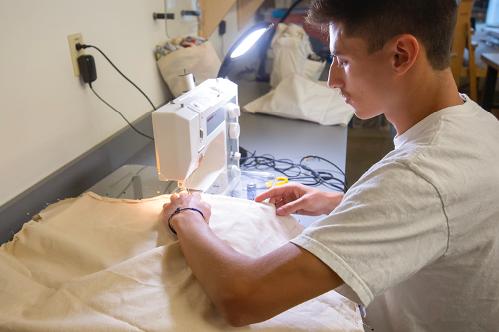 Student using sewing machine on white fabric.