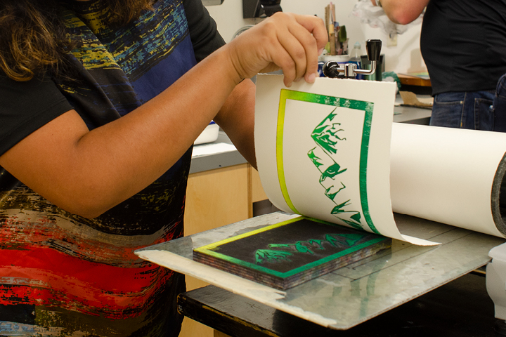 Student lifting green and yellow mountain scape print from wood block stamp.
